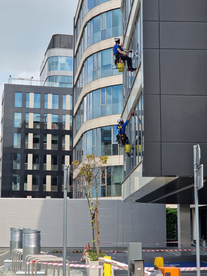 why-choose-us Two workers clean windows on a tall office building in a city setting.